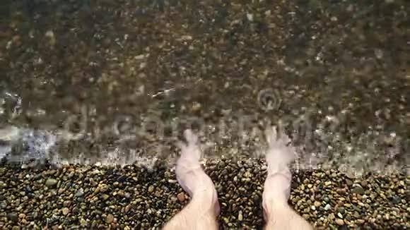 一个赤脚的人站在水中的一个鹅卵石海岸上水洗了他的脚相机的焦点在视频的预览图