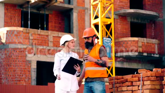 一个戴着白色头盔的女人和一个留胡子的男人在工地上交谈建设理念两个工程师视频的预览图