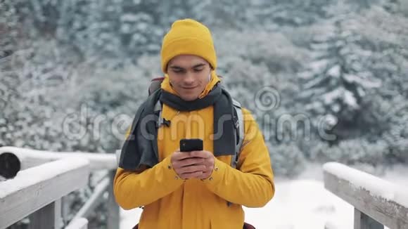 一位年轻的游客走在雪山上的一座桥上手里拿着一部智能手机通信社交网络视频的预览图