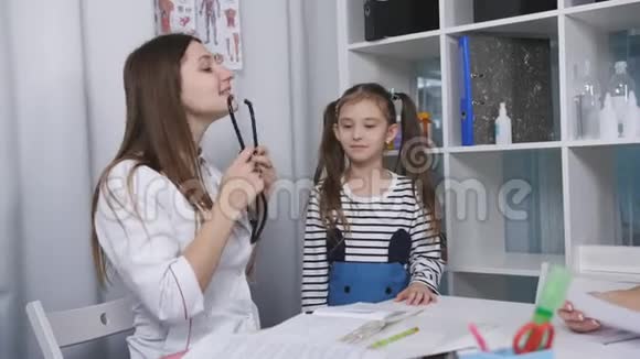 女医生在一家医疗诊所的办公室里听着带音响镜的小女孩说话视频的预览图