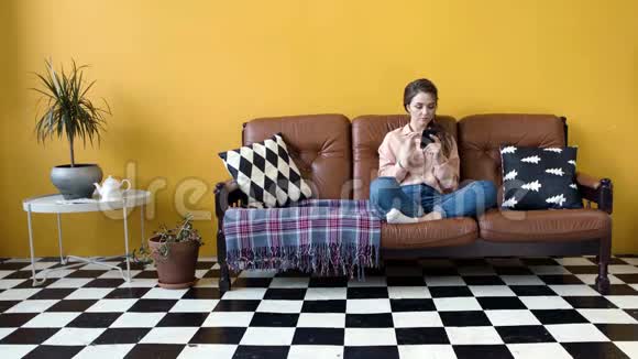 漂亮的年轻女人坐在沙发上打电话库存录像有魅力的女人在电话里翻新闻视频的预览图