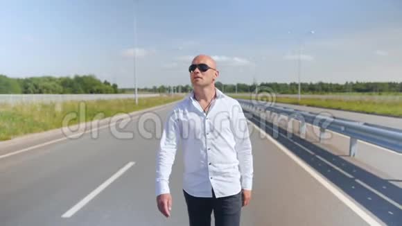 一个戴太阳镜的秃头男人在路上唱歌和散步的肖像全垒打视频的预览图
