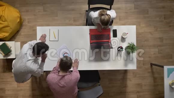 两个男人在讨论项目时女人在笔记本电脑上工作坐在现代办公室的桌子上视频的预览图