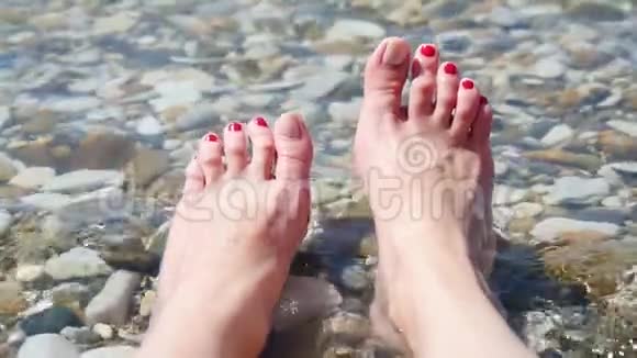 女孩正坐在鹅卵石海滩上享受着海水的冲浪女性腿部在水中特写这就是视频的预览图