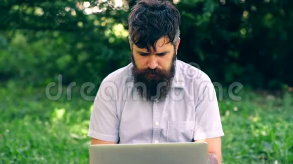 那个留胡子的人在公园里用笔记本电脑工作一个学生在草地上坐着情绪激动地用笔记本电脑工作视频的预览图