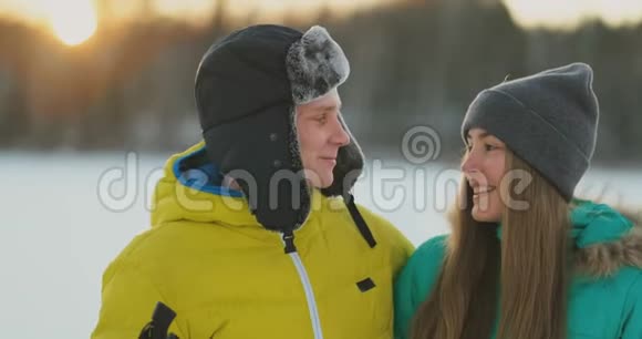 一个穿黄色夹克的男人和一个穿蓝色连衣裙的女孩在日落时慢动作滑雪视频的预览图