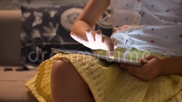 移动小女孩在平板电脑上玩游戏和坐在沙发上孩子使用小工具概念室内视频的预览图