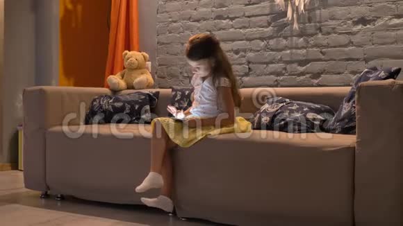小可爱的女孩坐在沙发上在平板电脑上打字现代客厅背景室内视频的预览图