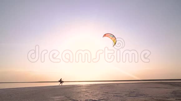 黎明背景下一个人的剪影控制着一只训练风筝沿着海滨散步视频的预览图