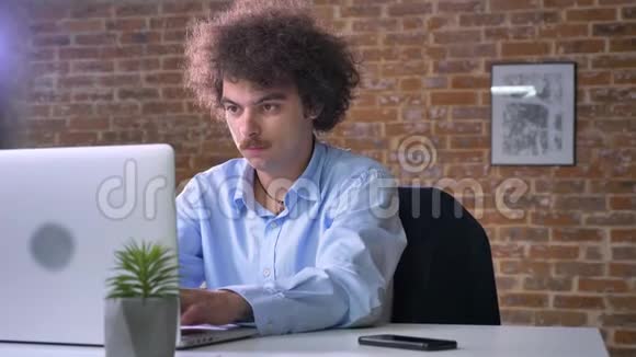 不快乐的商人在生意上有困难在笔记本电脑上工作拿着电话坐在现代化的办公室里视频的预览图