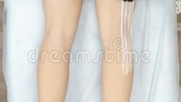 美容师在腿的背部涂抹和撕裂脱毛肿块的腿部特写视频的预览图