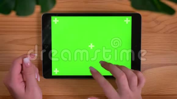 在木桌和植物背景上女性手触摸水平平板绿色屏幕的特写镜头视频的预览图