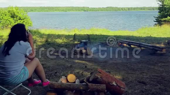一个女人坐在火边的河岸上弓手挂在上面视频的预览图