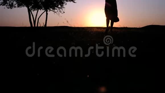 一个年轻美丽的女人在一片发光的草地上朝夕阳走来的剪影视频的预览图