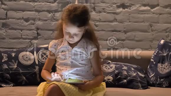 小女孩坐在沙发上在平板电脑上打字孩子在玩小玩意孩子在家里的概念在室内视频的预览图