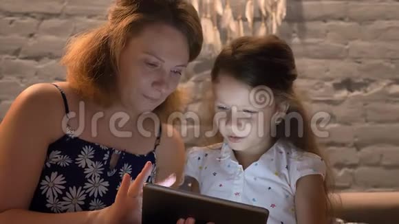 年轻的母亲小女儿拿着平板电脑坐在现代家庭的沙发上家庭观念户外视频的预览图