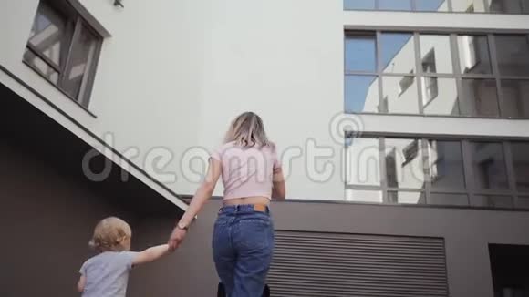 年轻的母亲和她的女儿绕着房子走走在街上视频的预览图