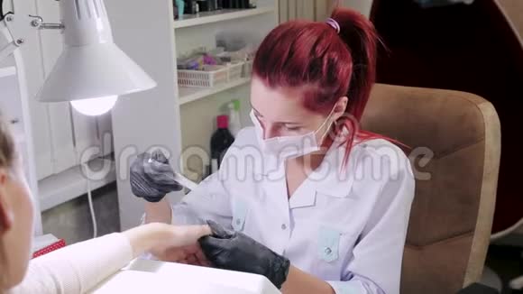 在美容院带手套的女美甲师在涂胶前用指甲锉钉客户视频的预览图