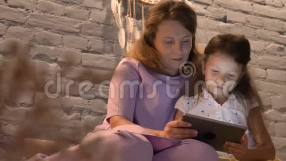 母亲和她的小女儿在平板电脑上玩游戏孩子笑着家庭观念和设备在室内视频的预览图