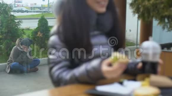 饥肠辘辘的流浪汉坐在街上快乐的女人在咖啡馆里咬着美味的汉堡视频的预览图