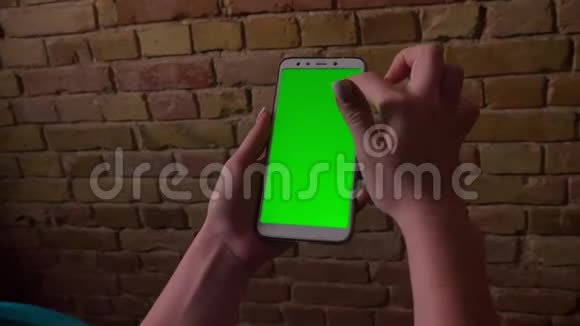 特写女性手触摸和滑动在绿色屏幕上的智能手机在布里肯墙背景上的肖像视频的预览图