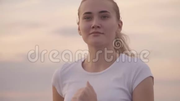 日落时分一个穿着白色t恤的女孩在从城市出发的路上奔跑头发在风中飘扬健康生活方式视频的预览图