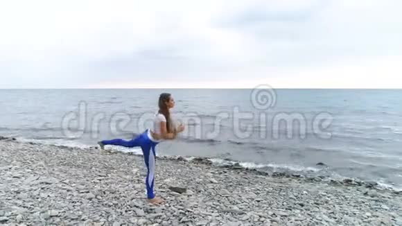 女孩正在做腿部运动在海洋和岩石背景上的呼吸练习中做身体反射空中录像视频的预览图