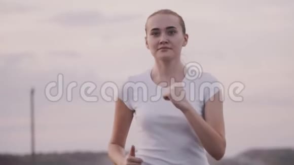 健康的生活方式运动女孩穿着白色t恤在跑道上跑步这个女孩在城外的路上跑视频的预览图