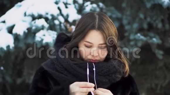 冬天在户外戴白色耳机的年轻女人穿着白色拉绳的年轻漂亮的女人视频的预览图