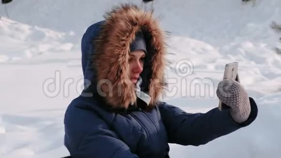 年轻快乐的美女打电话视频聊天在冬天的公园里在下雪的日子里在城市里下雪了侧视图视频的预览图