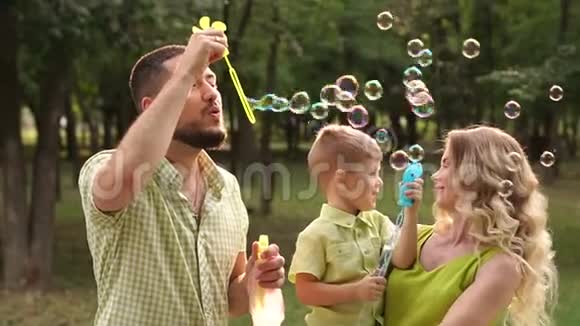 一个幸福的家庭和一个小儿子在公园里用肥皂泡的肖像慢节奏视频的预览图