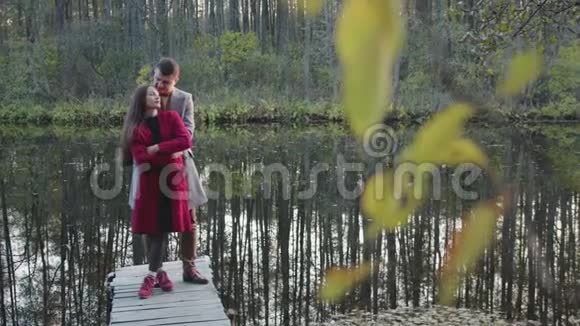 快乐年轻夫妇站着拥抱在湖边的木桥上接吻视频的预览图