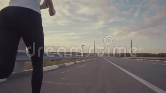 一个穿着白色t恤穿着明亮的运动鞋留着长发的运动女孩在城外的一条空跑道上奔跑视频的预览图