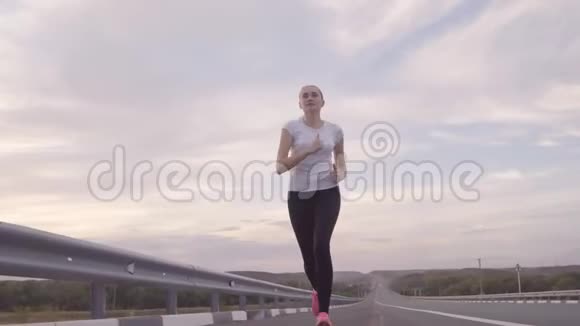 健康的生活方式一个穿着白色T恤和明亮运动鞋的女孩在日落时分从城市的道路上奔跑头发视频的预览图