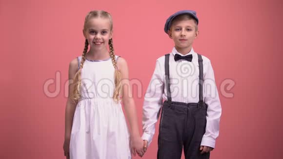 微笑的小男孩和女孩看着镜头手牵着粉红色的背景视频的预览图