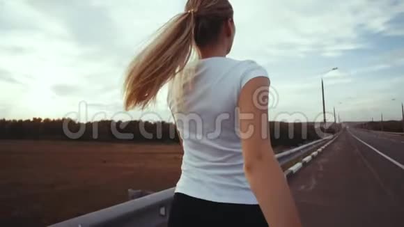 一个穿着白色t恤和长发的运动女孩沿着城外的一条空荡荡的跑着在休息的时候视频的预览图
