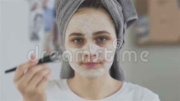 头上戴毛巾的女人戴上化妆面具看着镜头视频的预览图