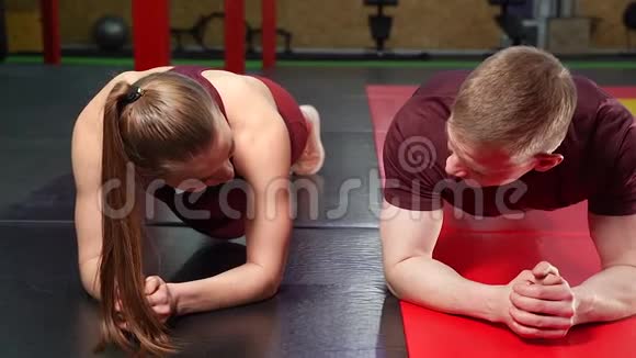 年轻夫妇躺在健身房的地板上做木板运动视频的预览图