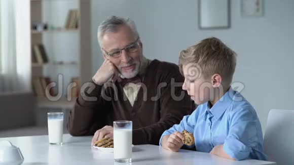 男孩吃带牛奶的饼干和爷爷分享幼儿园的消息视频的预览图