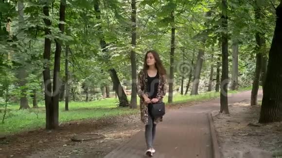 年轻迷人的女人穿着五颜六色的夹克在公园里散步绿树成荫环顾四周快乐而快乐视频的预览图