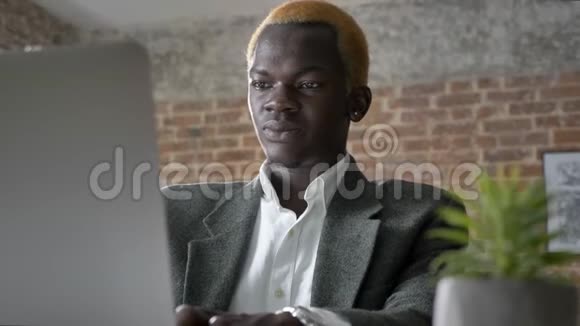 年轻的非洲金发商人在笔记本电脑上打字坐在现代办公室里自信地笑着视频的预览图