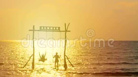 4K幸福夫妇的剪影喜欢在日落时间随着秋千在海上摇曳夏天的标志在上面快乐的夏天视频的预览图