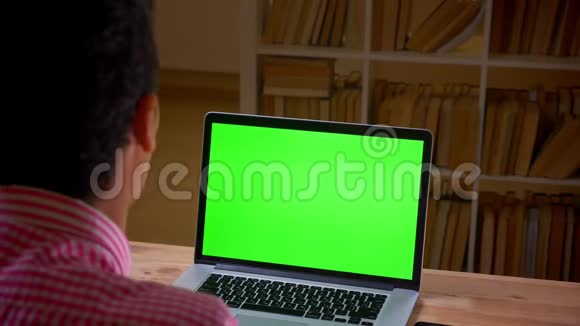 阿拉伯青年商人在办公室室内使用带有绿色屏幕的笔记本电脑的特写后景拍摄视频的预览图