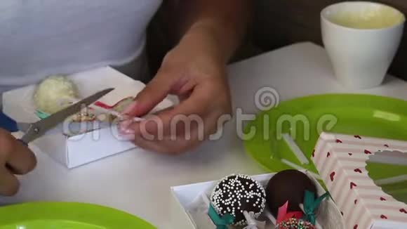 女人把蛋糕放在礼品盒里糖果装饰有不同颜色的敷料和丝带蝴蝶结修剪多余的剪刀视频的预览图