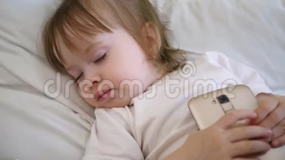 孩子躺在枕头上拿着药片可爱的婴儿睡在床上智能手机视频的预览图