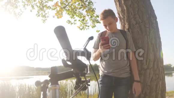 骑自行车后在公园里的男孩在日落时使用电话观看社交网络或聊天健康观念视频的预览图