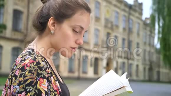 年轻美丽的女性阅读书籍坐在大学大楼附近的街道上集中精力和决心视频的预览图