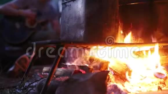 人们用篝火在金属桶里加热食物一个在后台弹吉他的男人视频的预览图