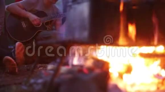 人们用篝火在金属桶里加热水一个在后台弹吉他的男人视频的预览图
