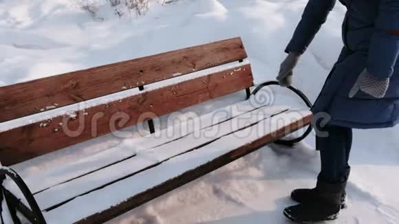 白天在大雪纷飞的天气里女人从冬天的城市公园的雪中清理长凳视频的预览图